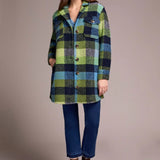 Woman wearing a green and blue plaid shirt over a blue top with jeans and brown boots on a beige background