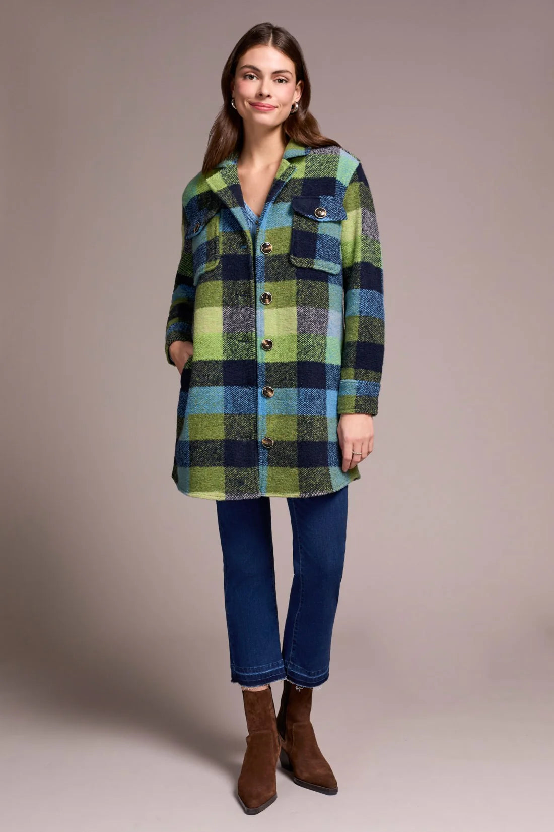 Woman wearing a green and blue plaid shirt over a blue top with jeans and brown boots on a beige background