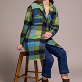 Woman wearing a plaid coat sitting on a wooden stool against a plain background