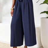 Person wearing a navy jumpsuit with wide-leg pants in a minimal indoor setting.