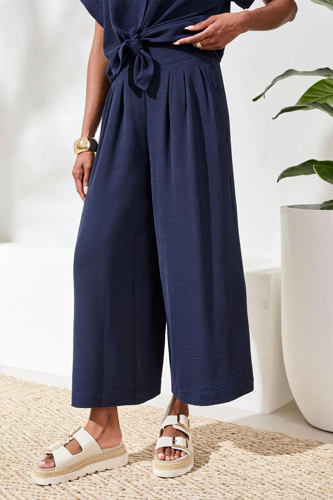 Person wearing a navy jumpsuit with wide-leg pants in a minimal indoor setting.