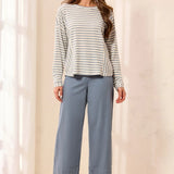 A woman modeling a long-sleeve striped knit top and wide-leg cropped pants in a softly lit indoor setting with curtains and a light floor.