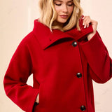 A woman wearing a bright red wool-blend coat with a wide collar and three dark buttons, paired with gray jeans, against a light beige textured wall.