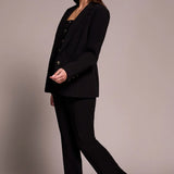 Woman wearing a black suit with leopard print shoes on a plain background