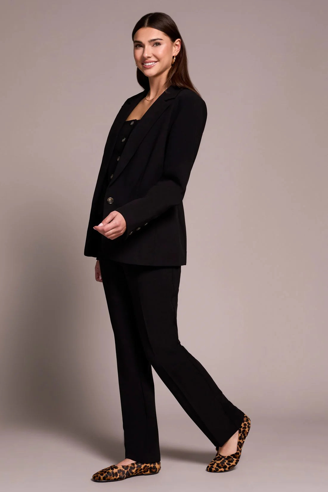 Woman wearing a black suit with leopard print shoes on a plain background
