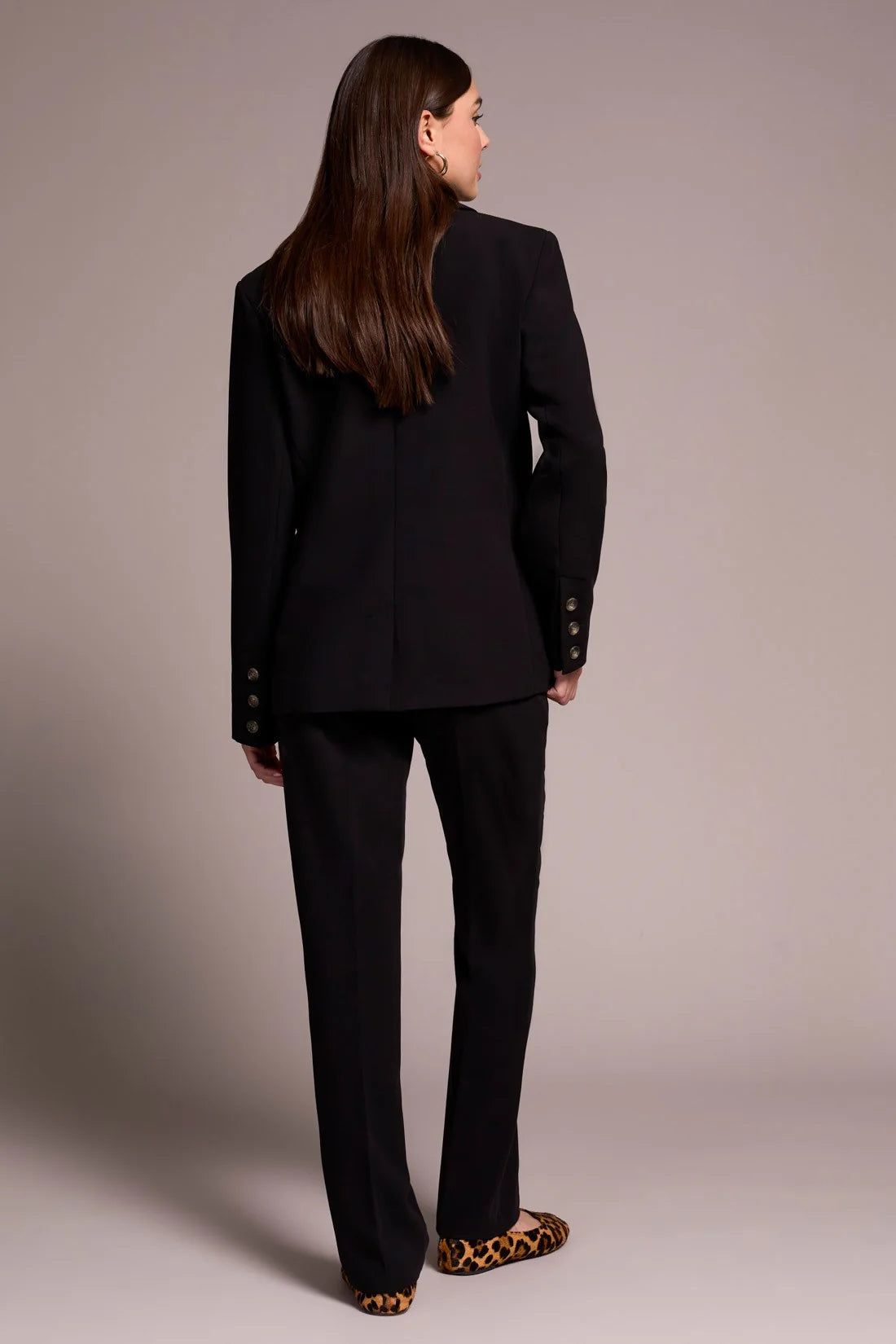 Woman wearing a black suit standing against a plain background