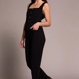 Woman wearing a black sleeveless jumpsuit with button details on a plain background