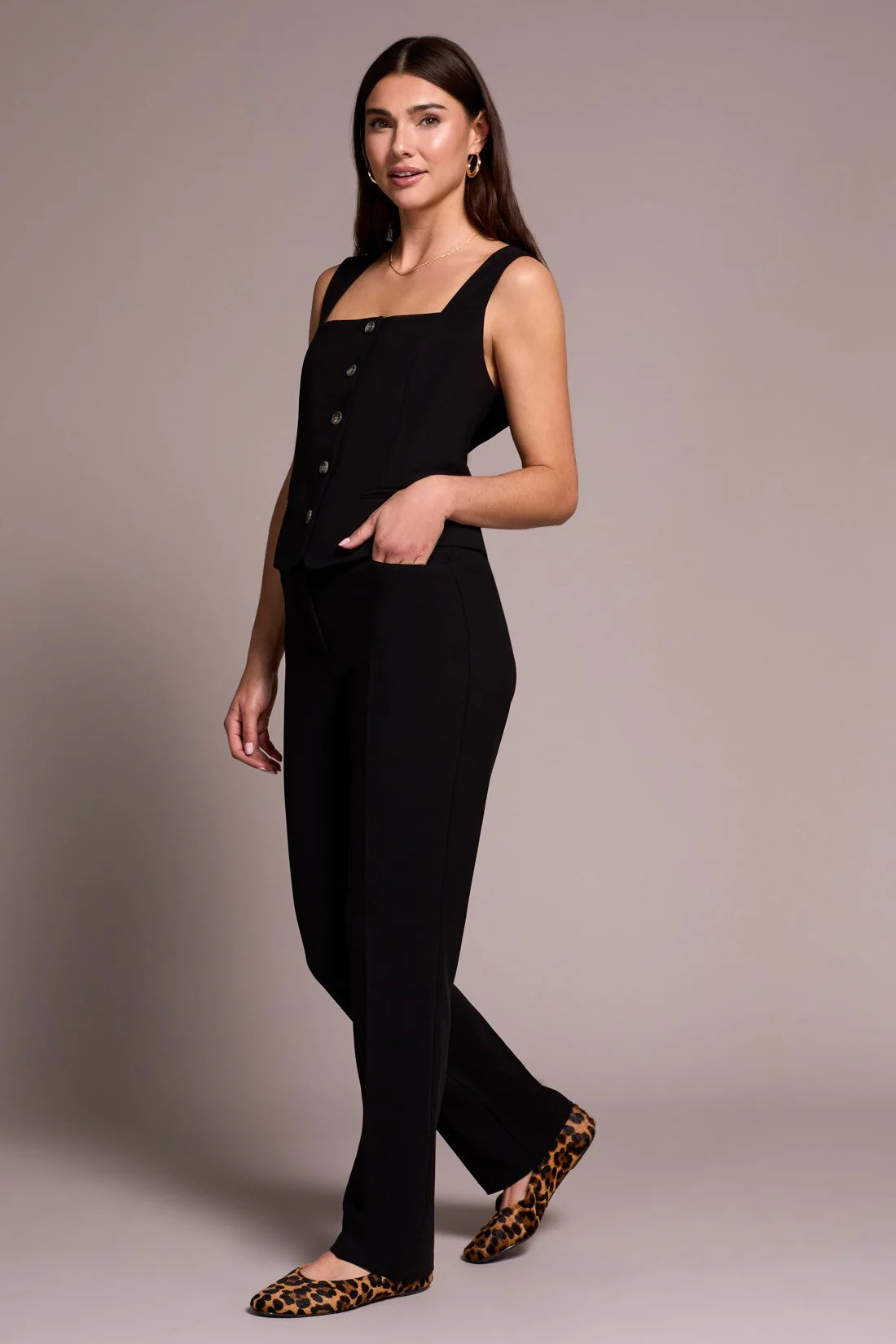 Woman wearing a black sleeveless jumpsuit with button details on a plain background