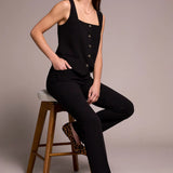 Woman sitting on a wooden stool wearing a black sleeveless top and pants with leopard print shoes.