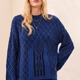 A woman wearing a textured royal blue cable-knit sweater with a diamond pattern, paired with matching blue pants, set against a neutral cream background.