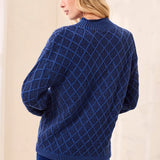 A woman shown from the back wearing a navy blue cable-knit sweater with a diamond lattice pattern and matching navy pants, set against a neutral cream-colored backdrop.