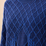 A close-up of a textured royal blue cable-knit sweater with a diamond pattern, worn by a model.