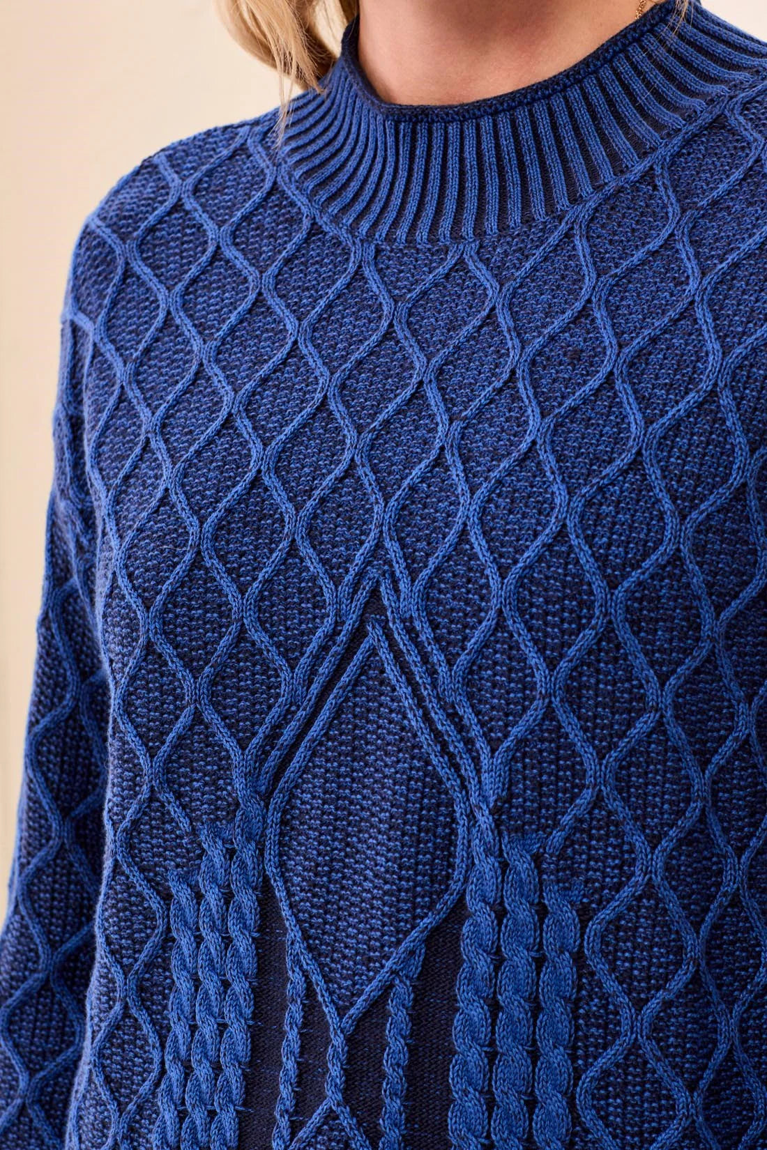 A close-up of a textured royal blue cable-knit sweater with a diamond pattern, worn by a model.