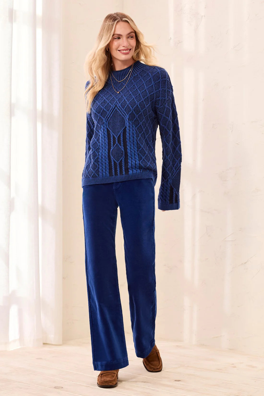 A woman modeling a matching navy blue knit sweater and wide-leg pants set, styled with brown suede shoes in a bright, neutral indoor setting.