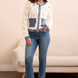 Woman wearing a white cardigan with blue accents and blue jeans standing in a room.