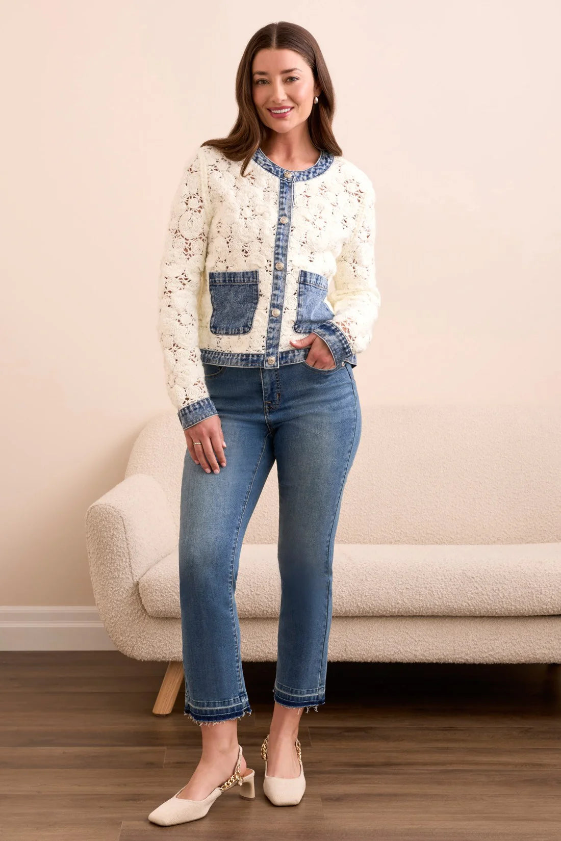 Woman wearing a white cardigan with blue accents and blue jeans standing in a room.