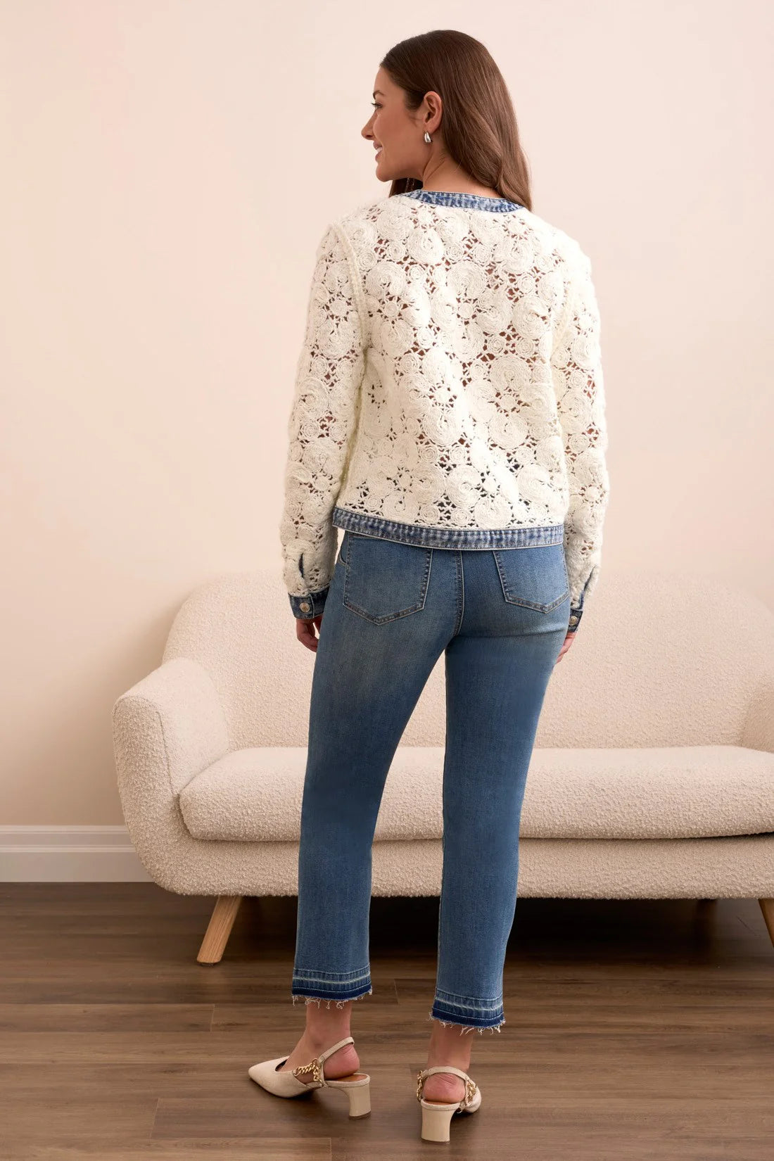 Woman wearing a floral blouse and blue jeans standing in a room with a beige sofa.