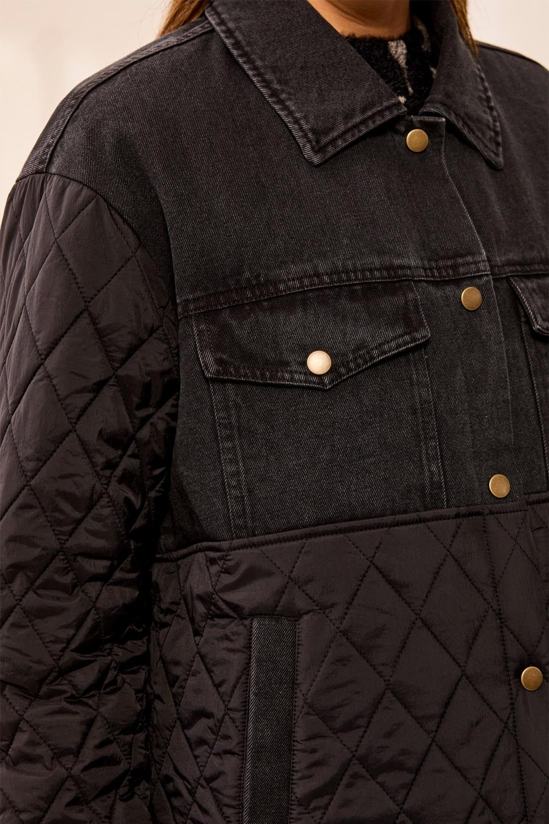 Close-up of a black quilted jacket with gold buttons on a neutral background