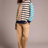 Woman wearing a striped sweater and beige pants against a plain background