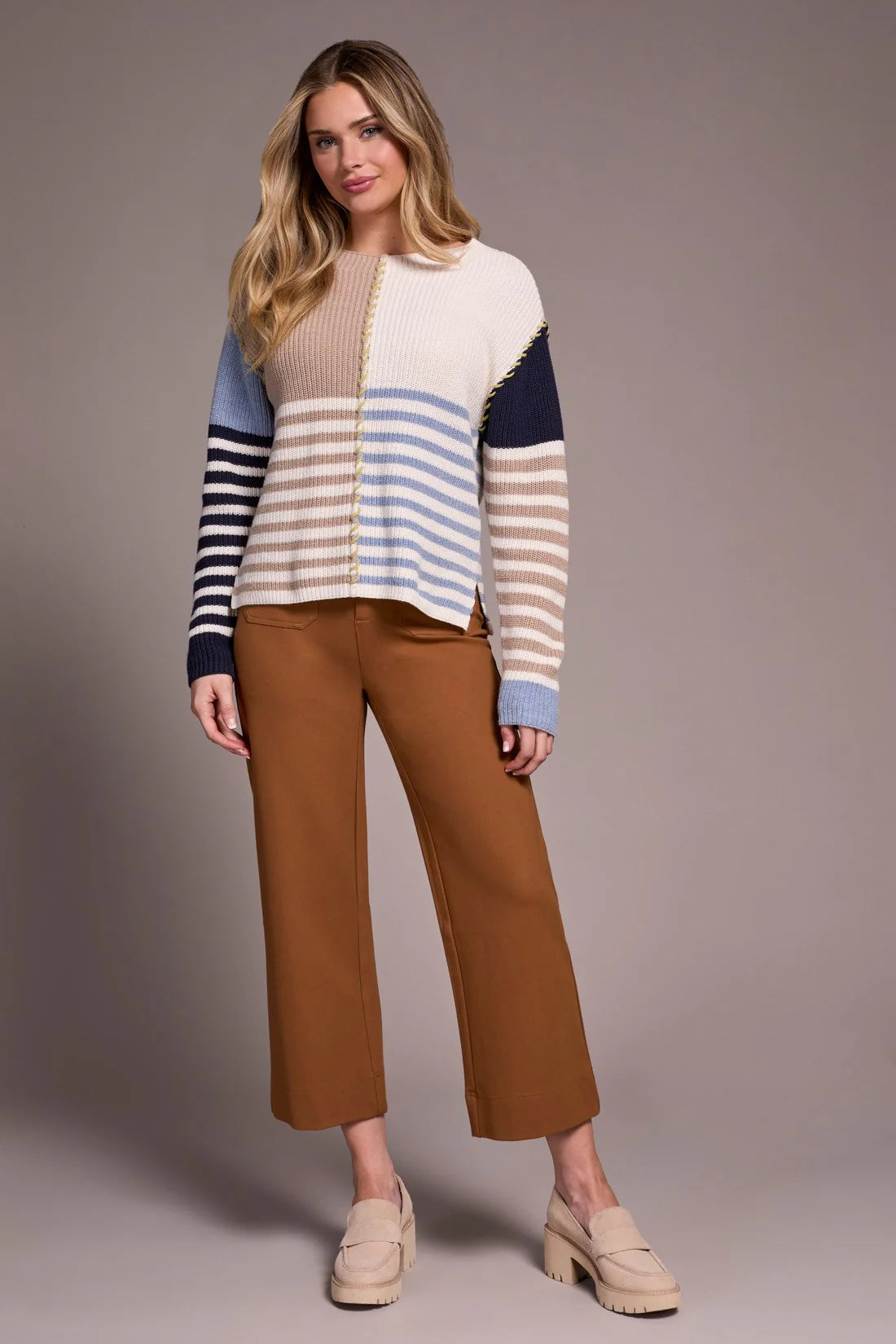 Woman wearing a striped sweater and brown pants against a plain background