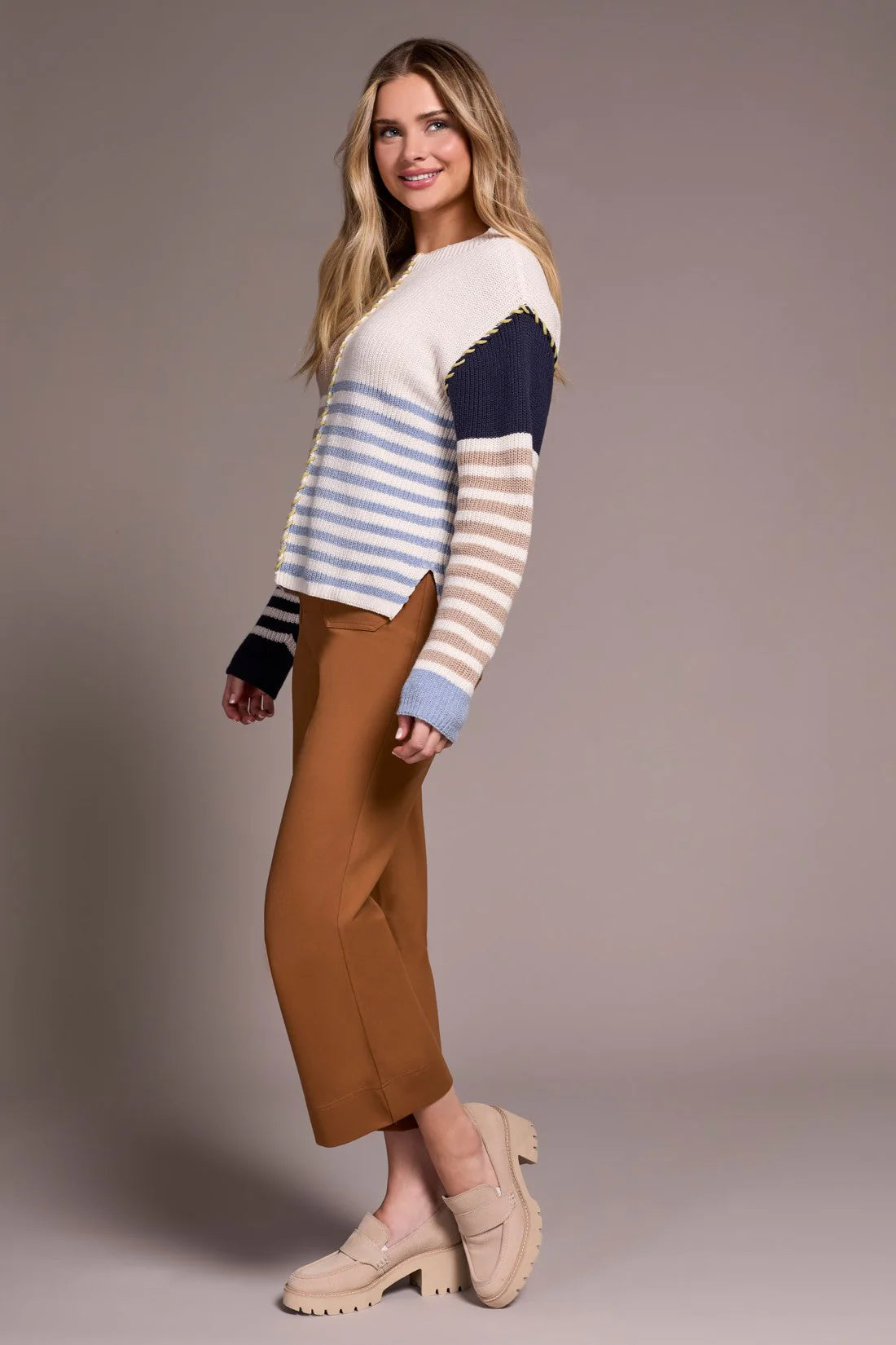 Woman wearing a striped sweater and brown pants against a plain background