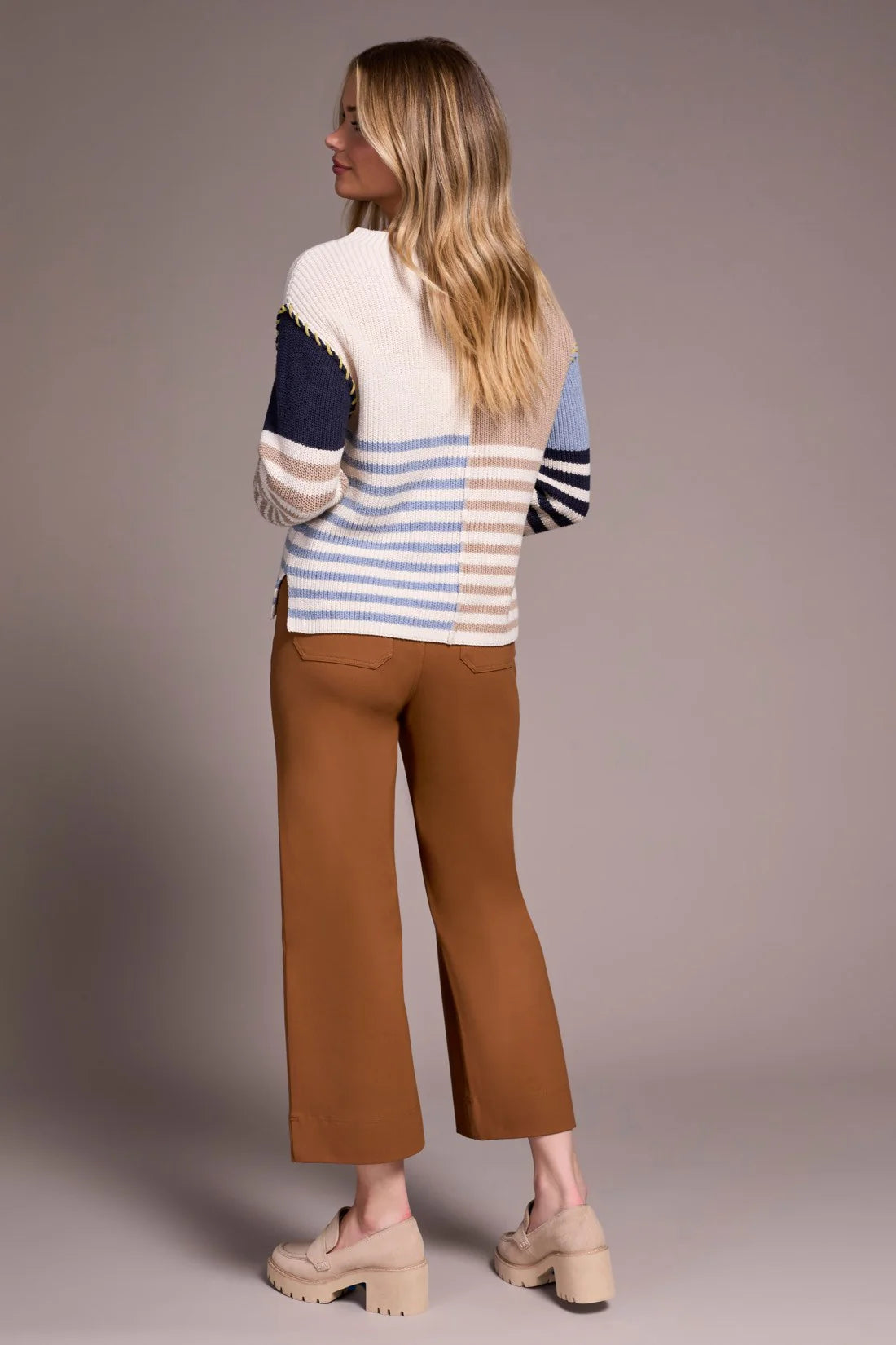 Woman wearing a colorful sweater and brown pants against a plain background