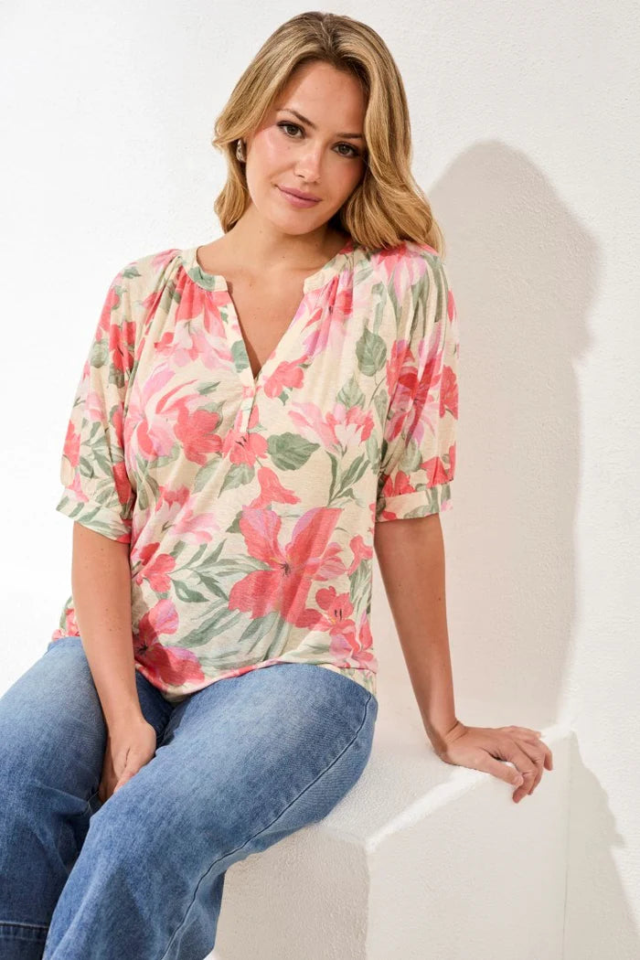 Woman wearing a floral top and jeans sitting on a white chair against a white background