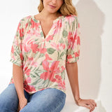 Woman wearing a floral top and jeans sitting on a white chair against a white background
