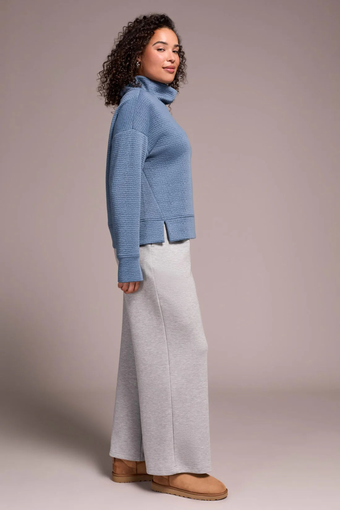 Woman wearing a blue sweater and gray pants against a plain background