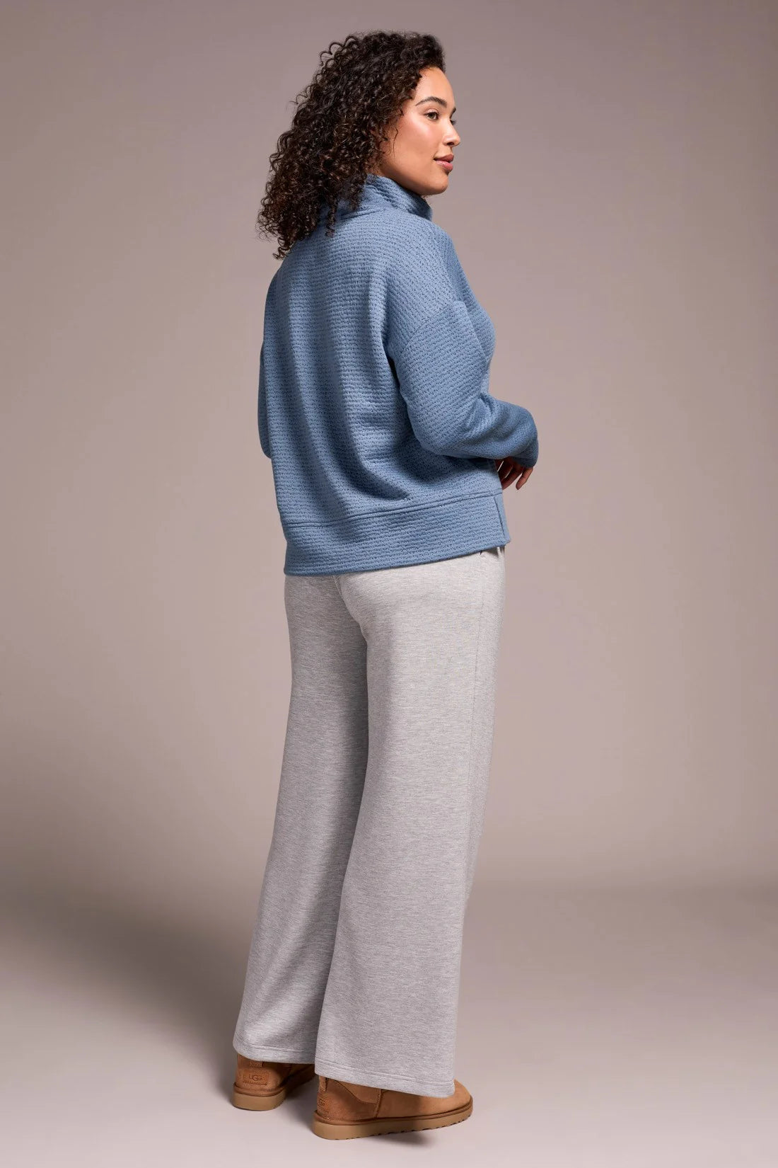 Woman wearing a blue sweater and gray pants against a beige background