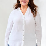 Woman wearing a white button-up shirt and light blue jeans against a plain background