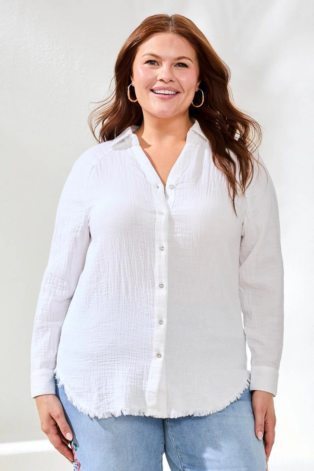 Woman wearing a white button-up shirt and light blue jeans against a plain background