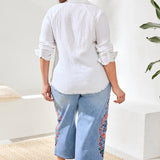 Woman wearing a white blouse and light blue jeans with floral patterns indoors.