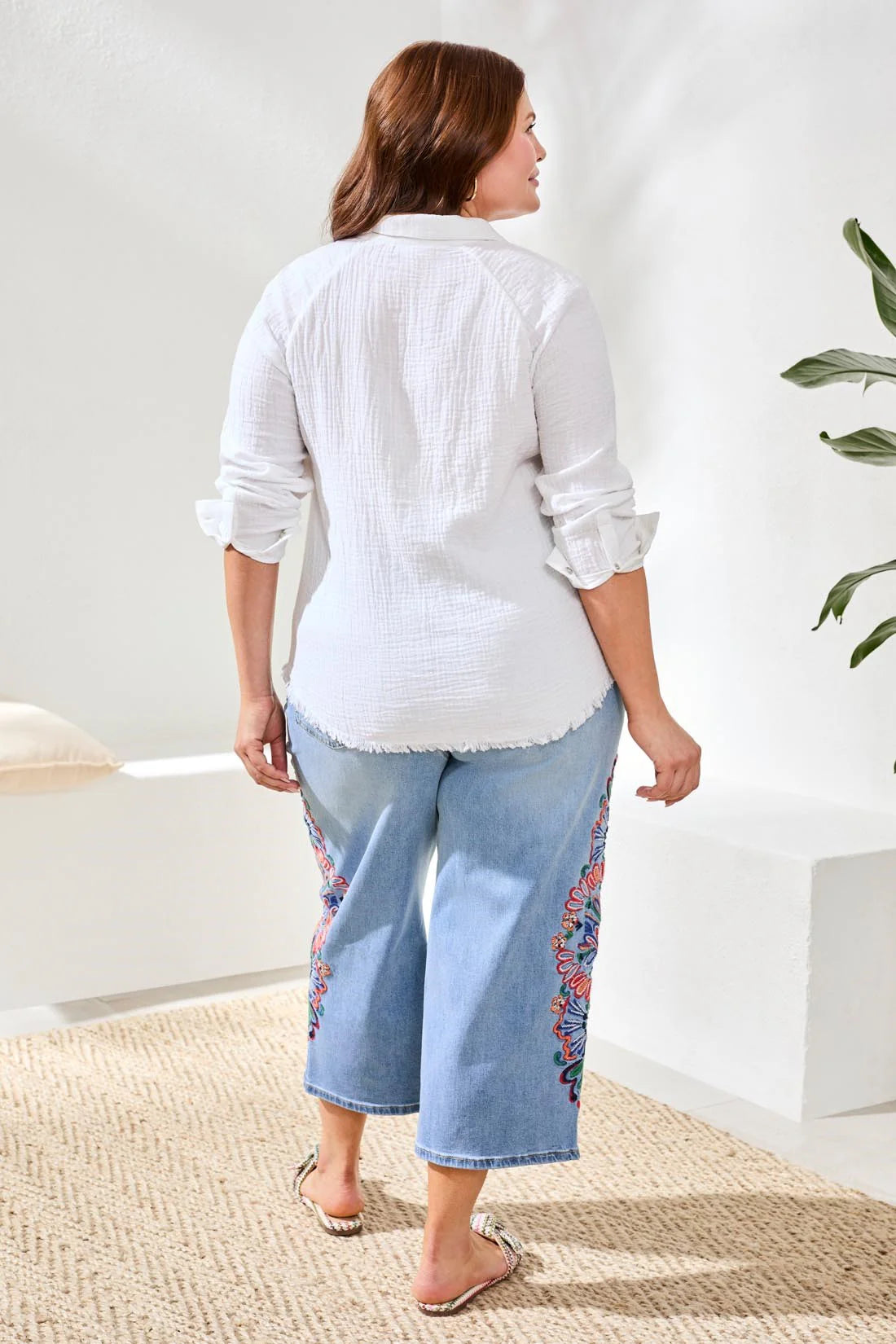 Woman wearing a white blouse and light blue jeans with floral patterns indoors.
