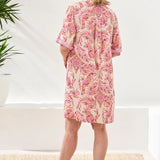 Woman wearing a pink floral dress standing in a minimal indoor setting.