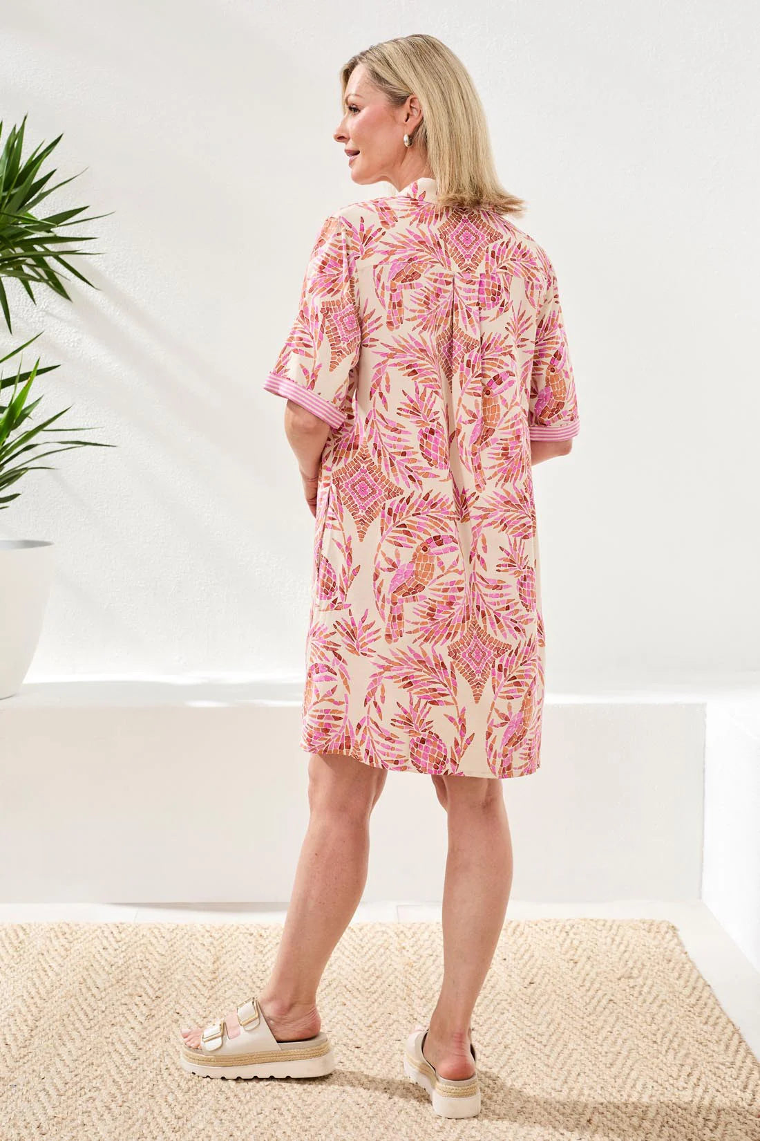Woman wearing a pink floral dress standing in a minimal indoor setting.