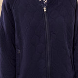 A close-up of a person wearing a navy quilted zip-up jacket over a patterned top. The jacket has a diamond-quilted texture, a full front zipper, and a stand collar.
