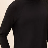 A close-up of a woman wearing a black ribbed knit turtleneck sweater against a light beige background.