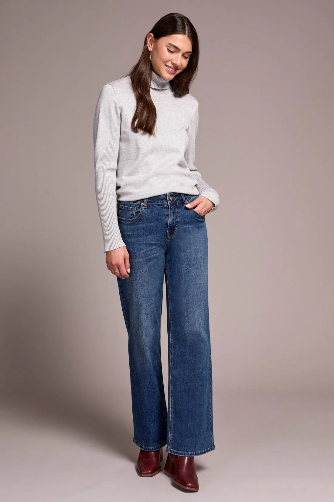 Woman wearing a white turtleneck sweater and blue jeans against a plain background