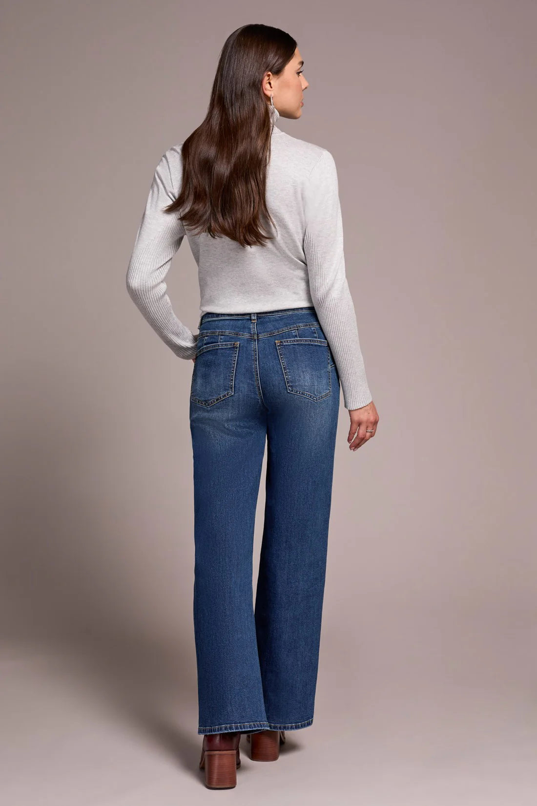 Woman wearing blue jeans and a light gray top against a plain background