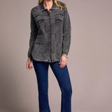 Woman wearing a gray textured jacket, blue jeans, and black boots on a beige background