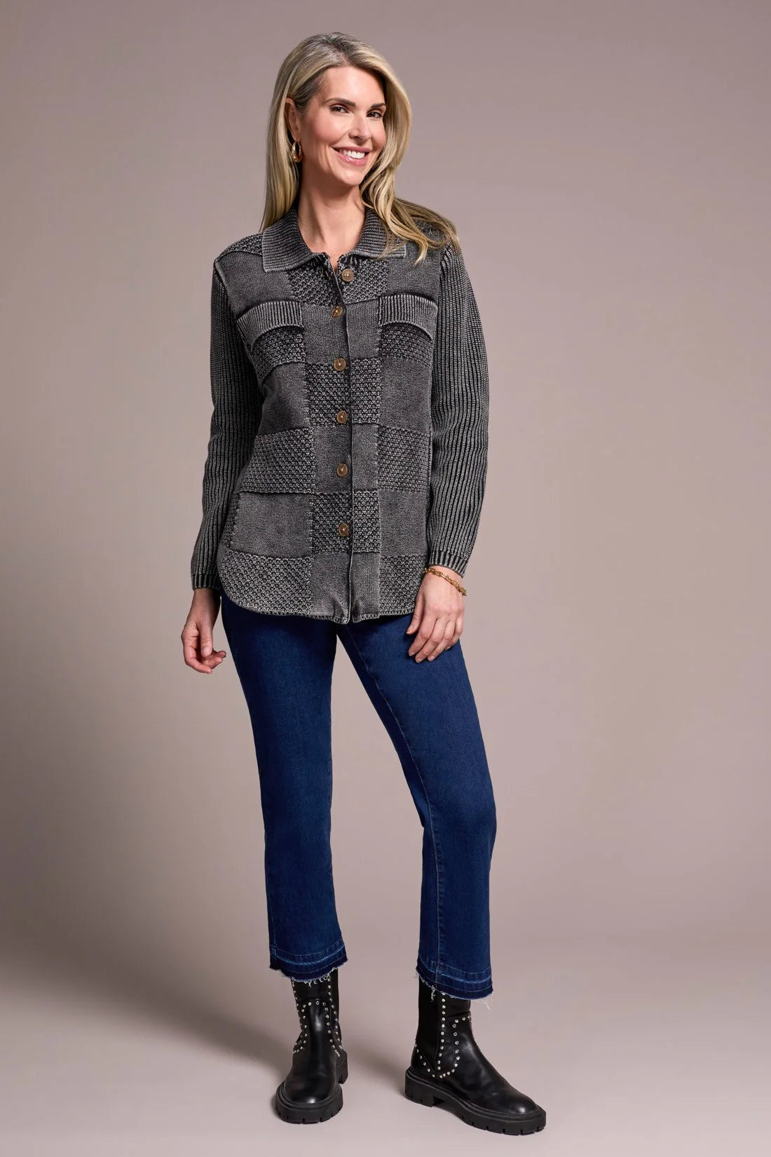 Woman wearing a gray textured jacket, blue jeans, and black boots on a beige background