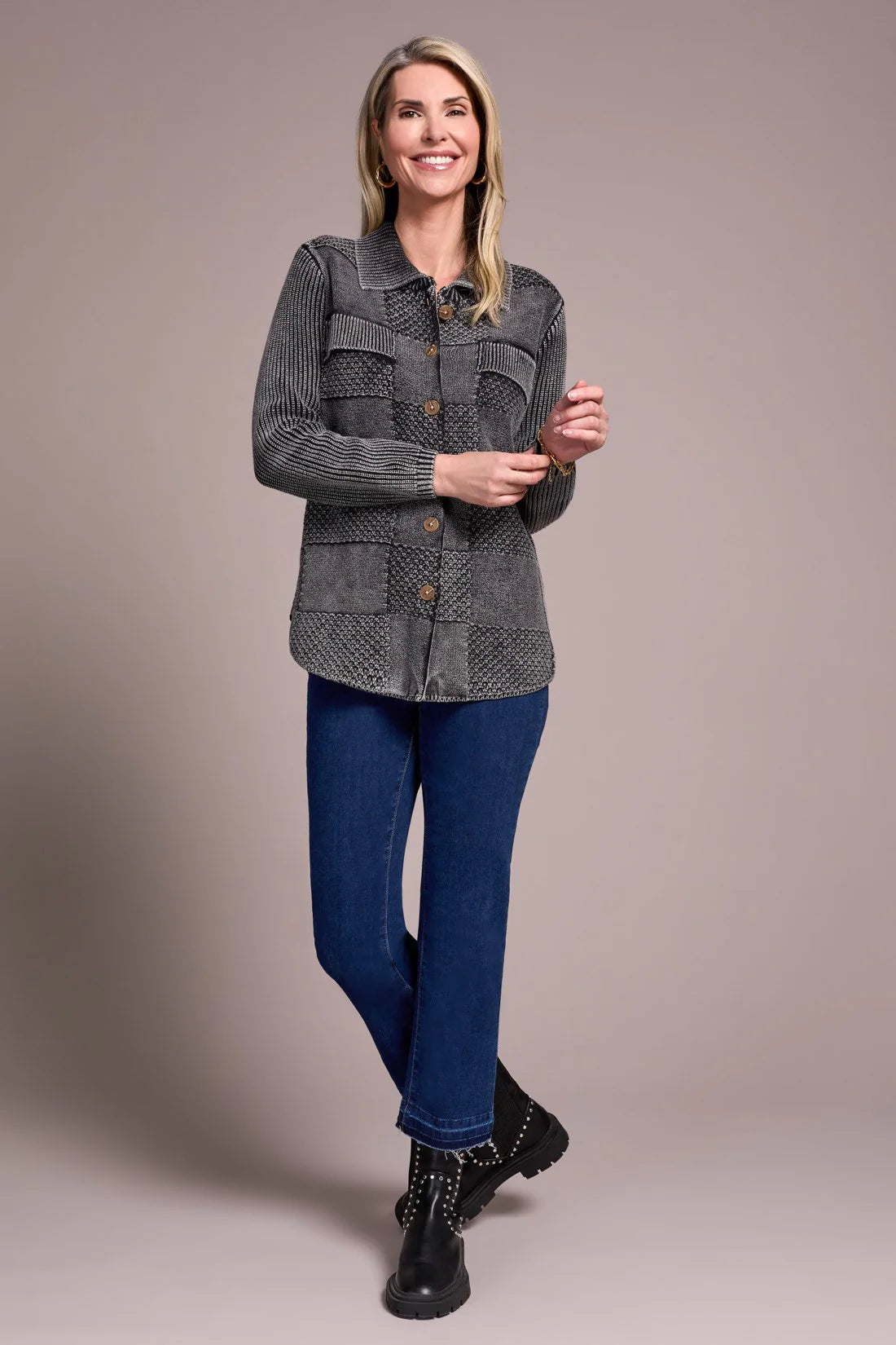 Woman wearing a gray quilted jacket and blue jeans against a beige background