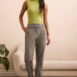 Woman wearing a green sleeveless top and gray checkered pants standing in a room with a beige sofa and plant.