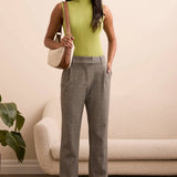 Woman wearing a green sleeveless top and gray pants, standing in a room with a beige sofa and plant.
