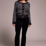 Woman wearing a black and gray patterned cardigan over a black top and pants on a plain background