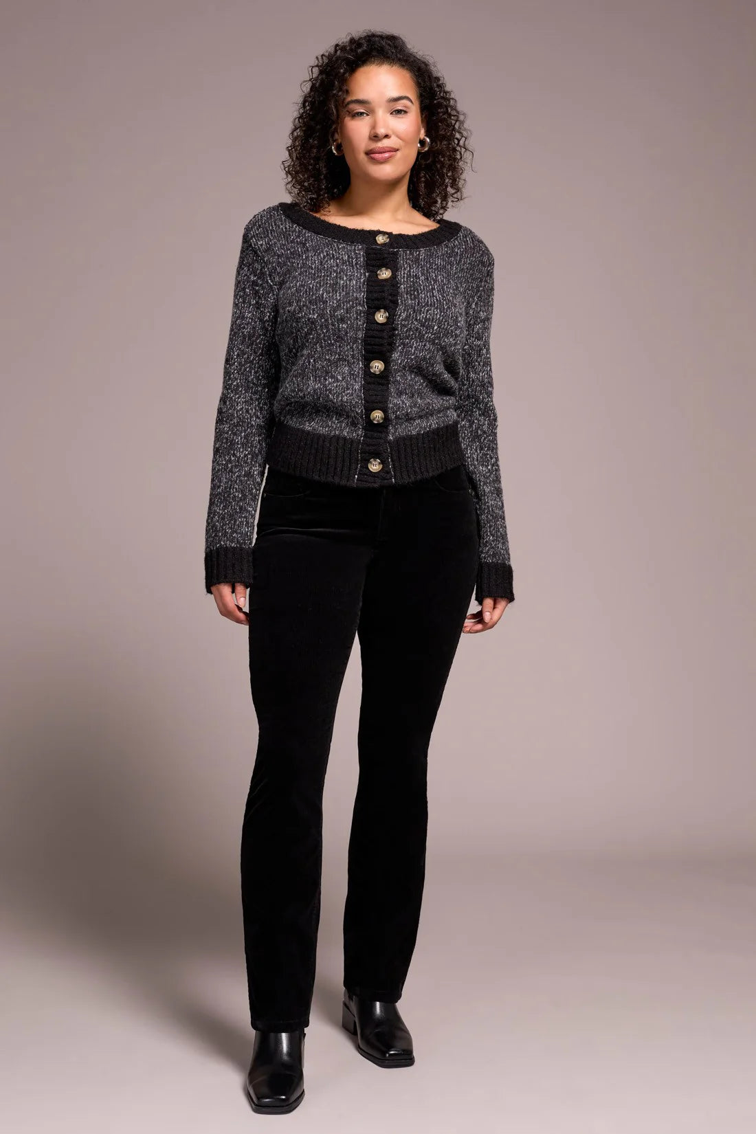 Woman wearing a black and gray patterned cardigan over a black top and pants on a plain background