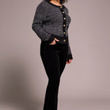 Woman wearing a gray cardigan with black buttons over a black top and black pants on a plain background