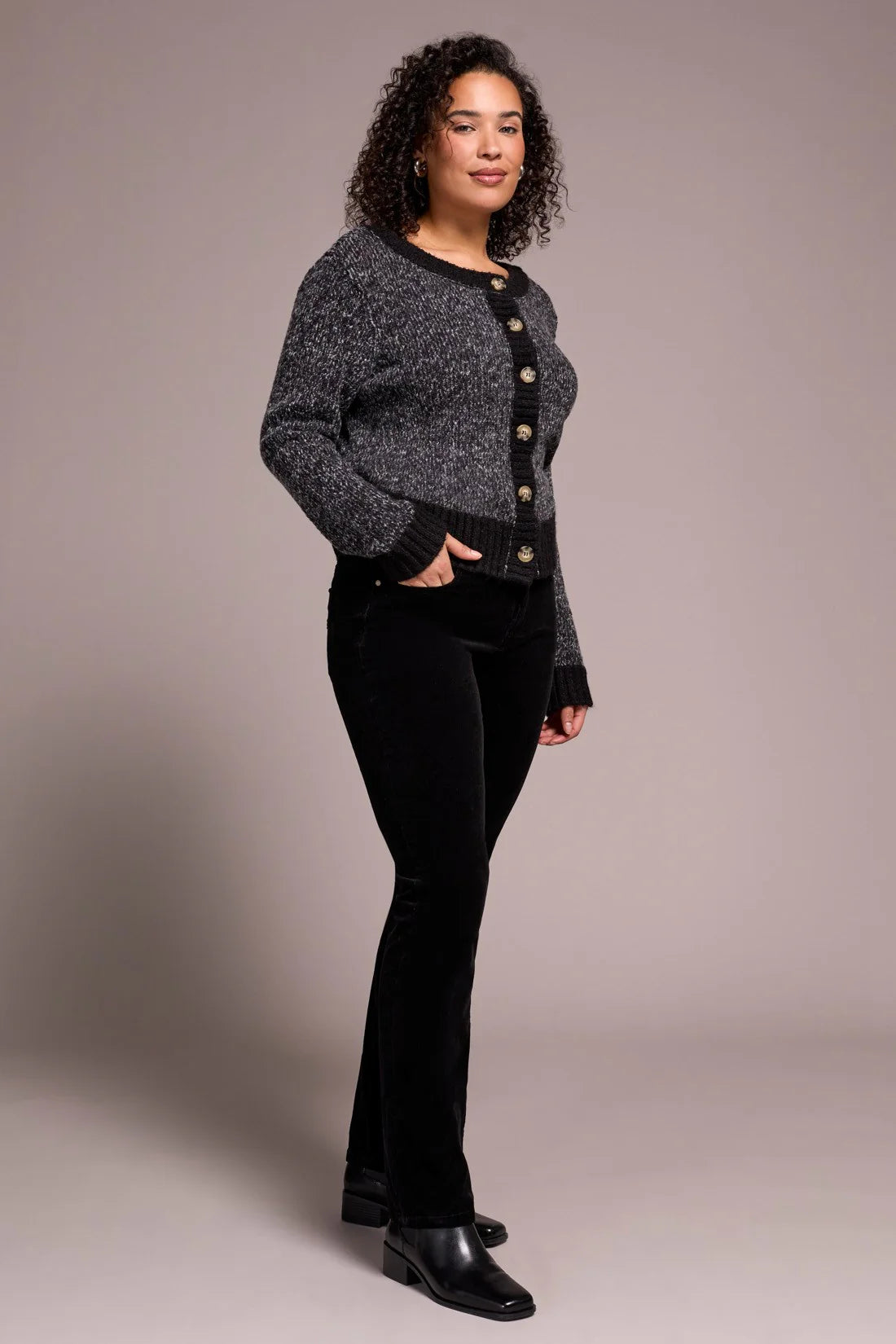 Woman wearing a gray cardigan with black buttons over a black top and black pants on a plain background