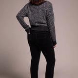 Person wearing a gray knitted sweater and black pants against a beige background